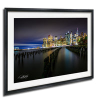 A nighttime cityscape with illuminated skyscrapers and a body of water in the foreground.