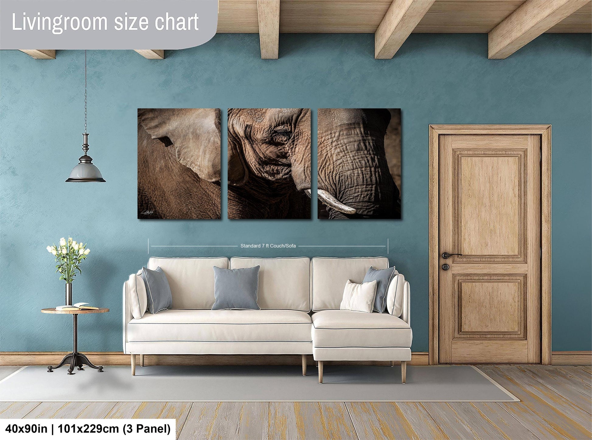 The image is a living room with a white sofa, a wooden door, and a wall with a large painting of an elephant. The painting is divided into three panels, and the wall is painted a light blue color.