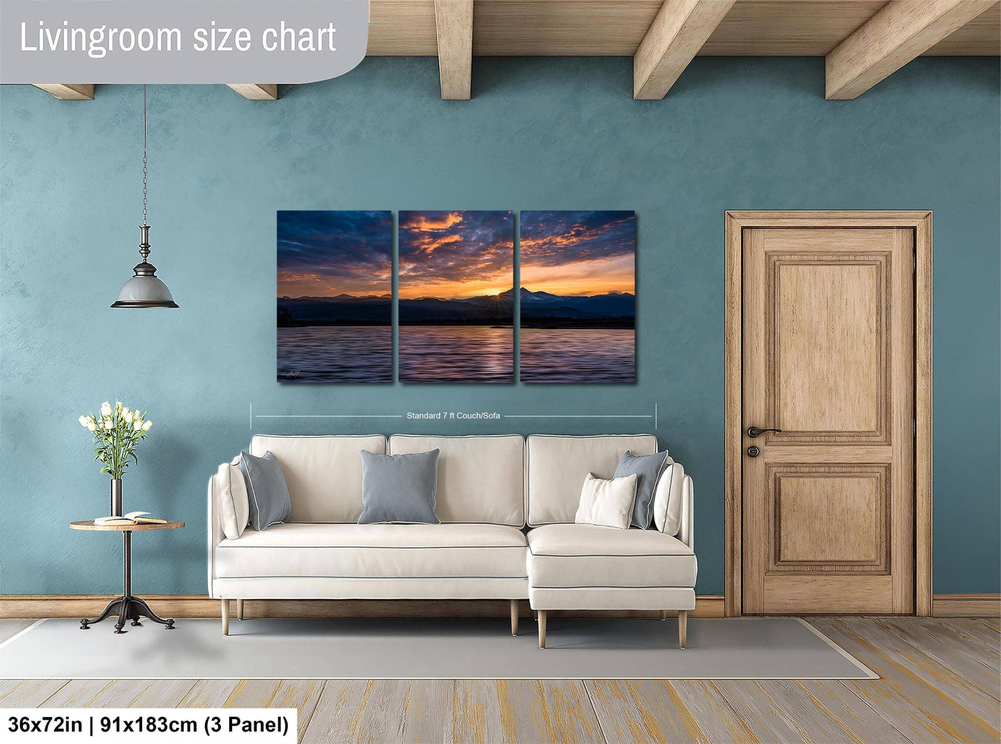 The image is a living room with a large white sofa, a wooden door, and a painting of a sunset over a body of water. The painting is divided into three panels, and the wall behind the sofa is painted a light blue color.