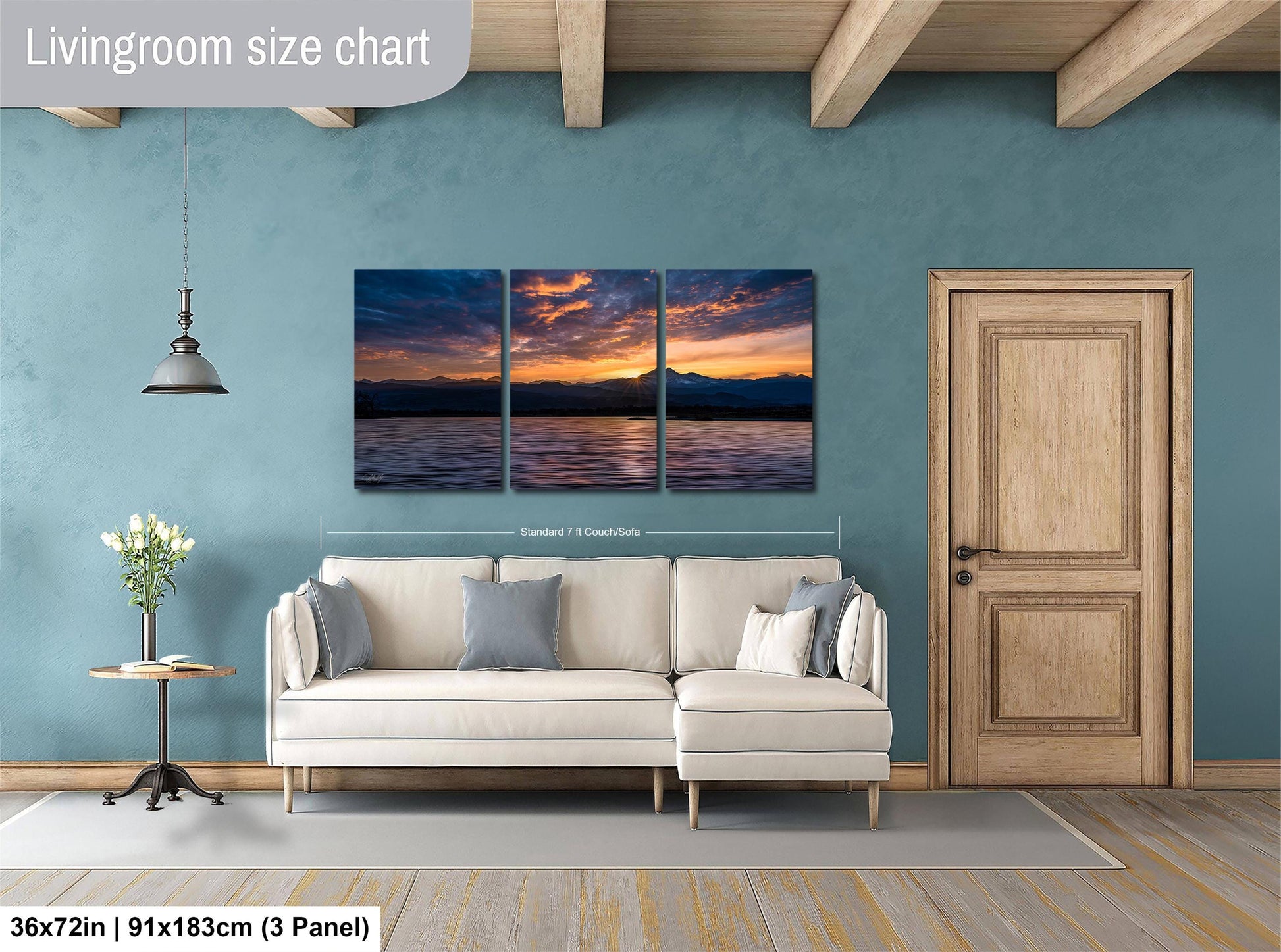 The image is a living room with a large white sofa, a wooden door, and a painting of a sunset over a body of water. The painting is divided into three panels, and the wall behind the sofa is painted a light blue color.
