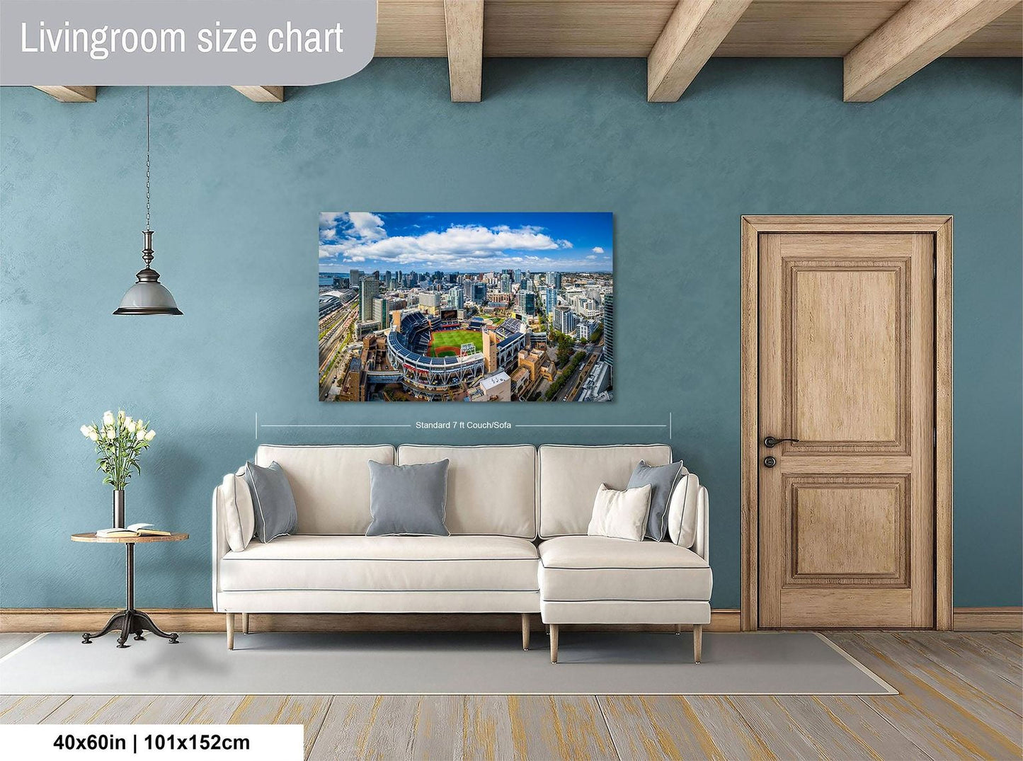 a living room with a large wall-mounted painting depicting a cityscape, a white sofa, a wooden door, and a small table with a vase of flowers.