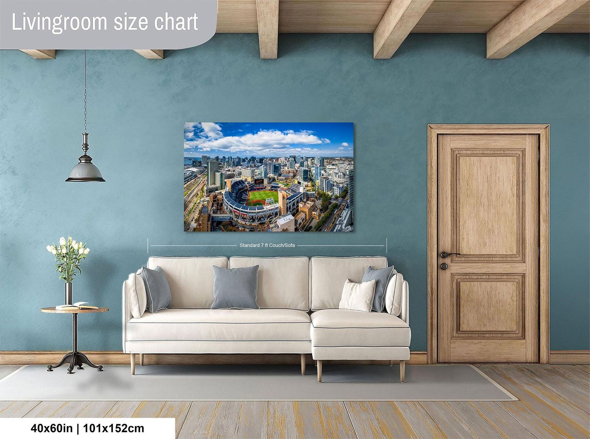 a living room with a large wall-mounted painting depicting a cityscape, a white sofa, a wooden door, and a small table with a vase of flowers.