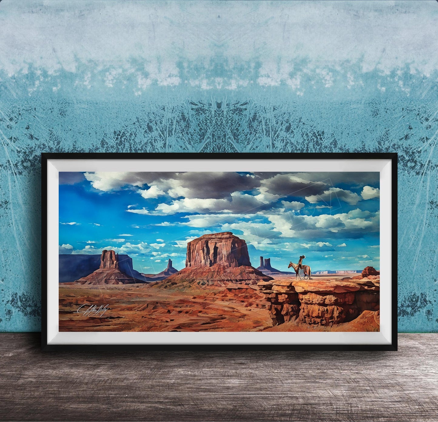 A framed painting depicting a scenic desert landscape with a person riding a horse in the foreground, set against a backdrop of mountains and a blue sky with clouds.