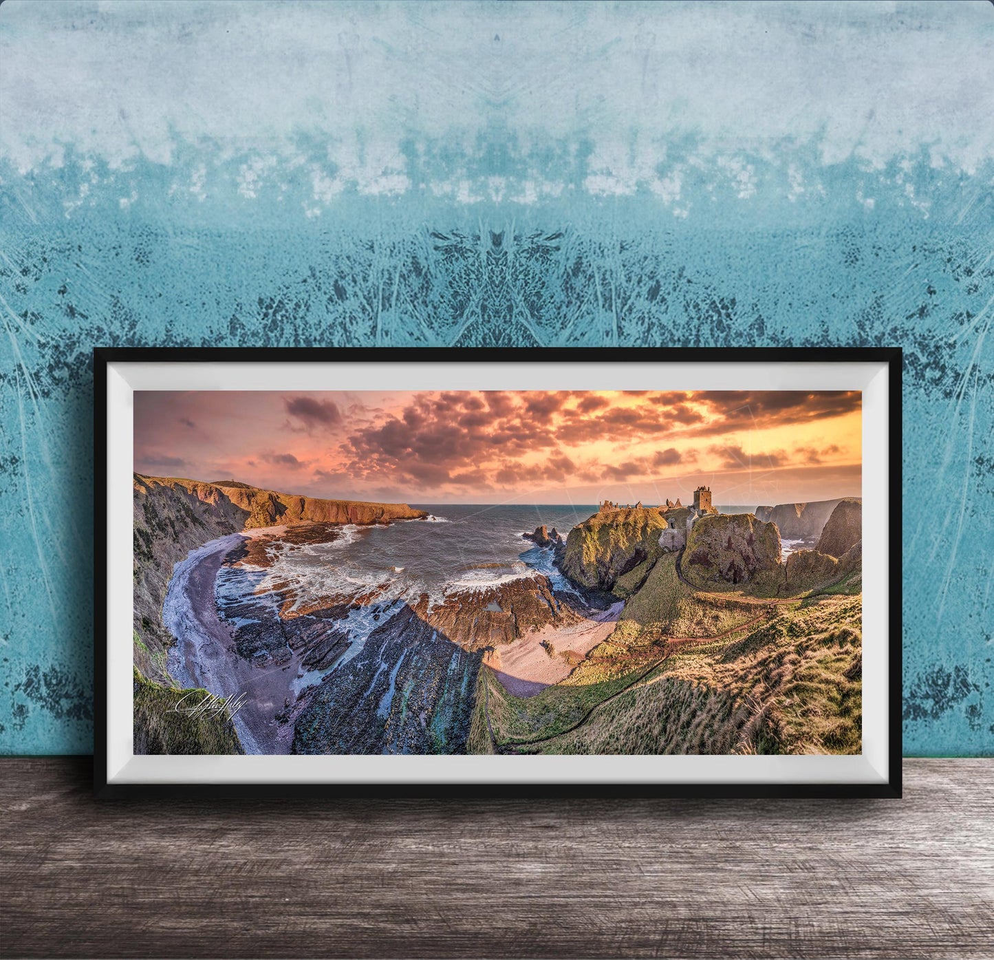 The image is a framed photograph of a scenic coastal landscape with rugged cliffs, a rocky shoreline, and a dramatic sunset over the ocean.