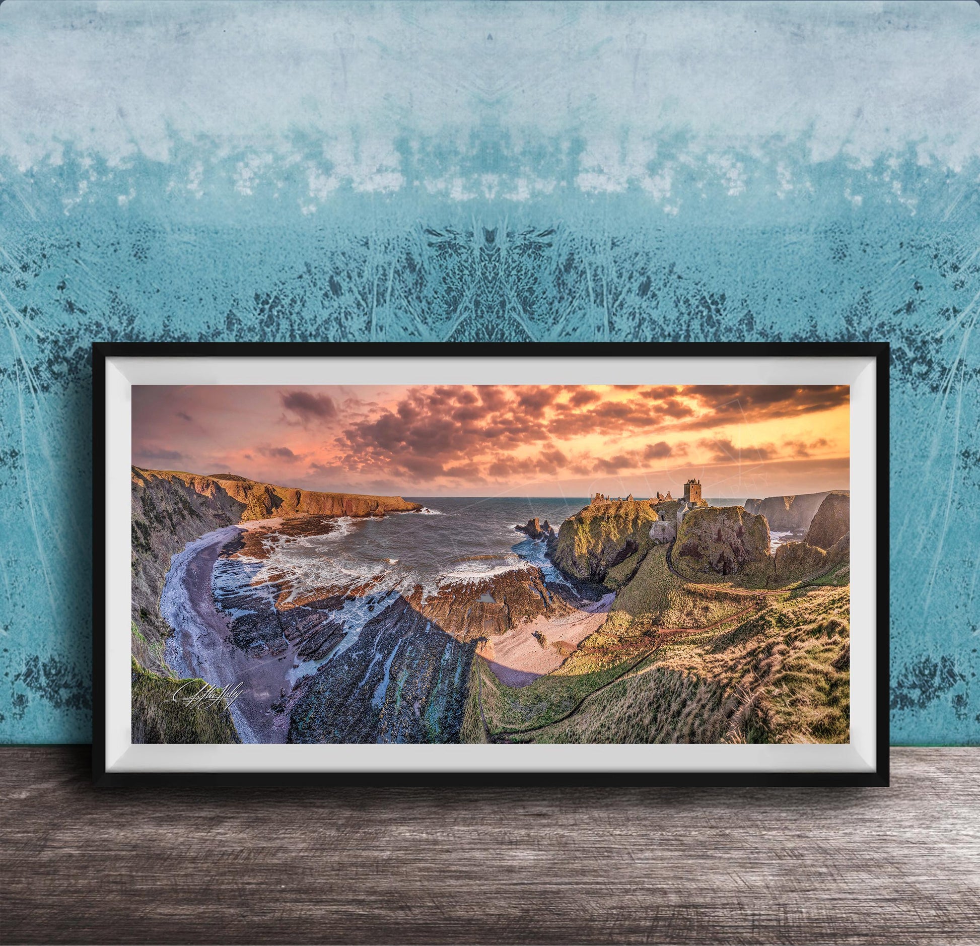 The image is a framed photograph of a scenic coastal landscape with rugged cliffs, a rocky shoreline, and a dramatic sunset over the ocean.