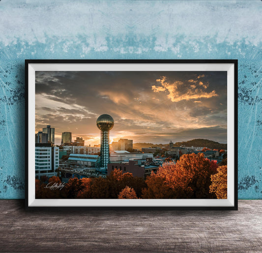a city skyline at sunset, with a large tower in the center and a colorful sky in the background.