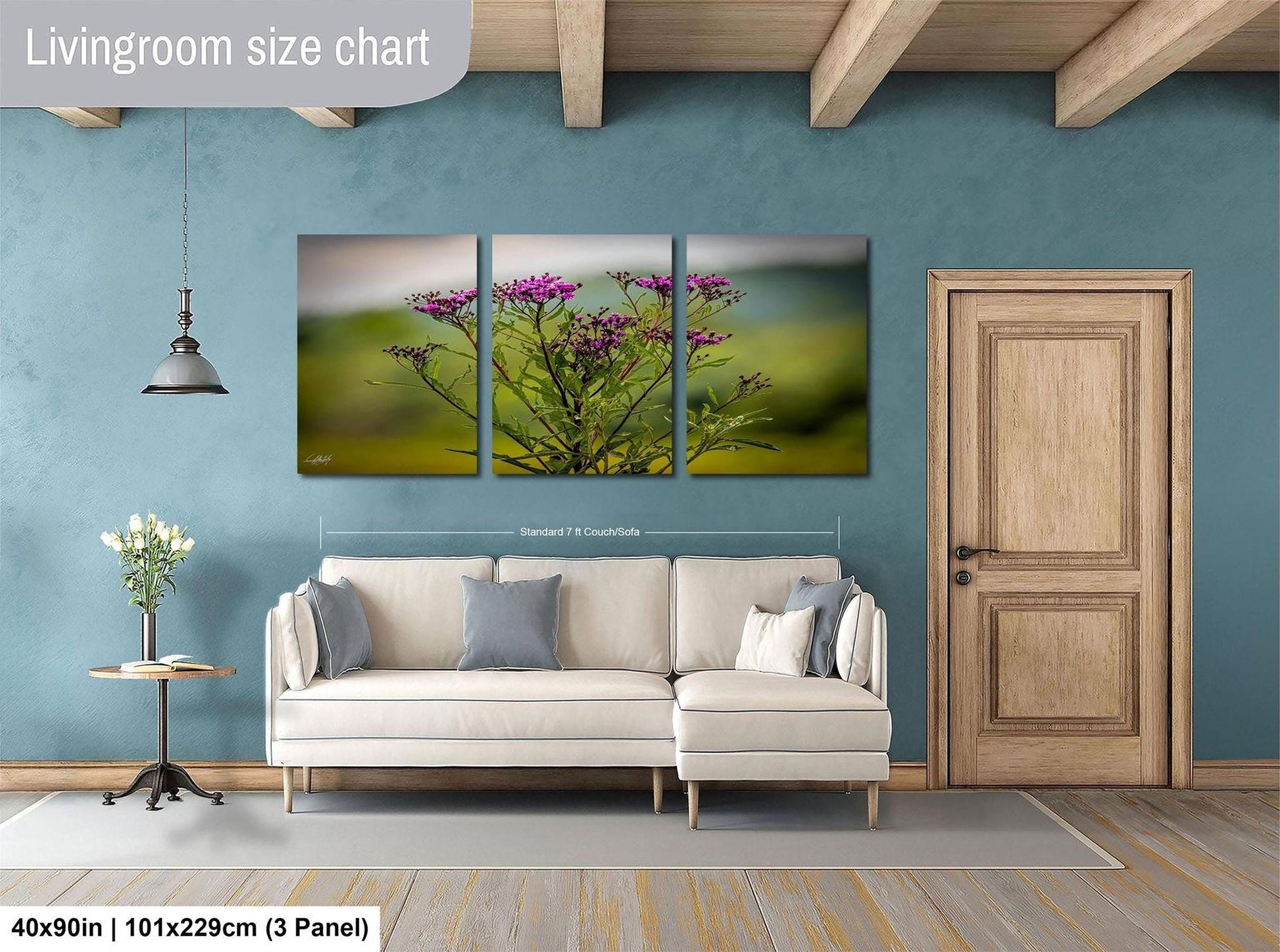 The image is a living room with a large white sofa, a wooden door, and a painting of a field of flowers hanging on the wall.