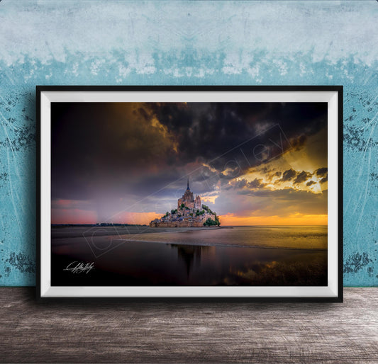 A framed photograph depicting the iconic Mont Saint-Michel island at sunset, with the island's reflection visible in the calm waters below.
