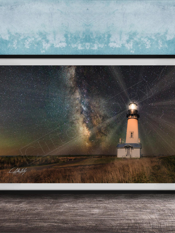 A framed photograph depicting a lighthouse standing in a field at night, with a starry sky and a galaxy in the background.