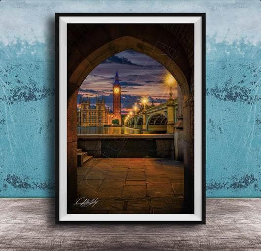 a cityscape at night, with a clock tower and a bridge visible in the background. The clock tower is illuminated, and the bridge is lit up, creating a warm and inviting atmosphere. The scene is framed in a black frame, which contrasts with the blue wall in the background. The image is a collage of multiple images, and the artist's signature is visible in the bottom right corner.