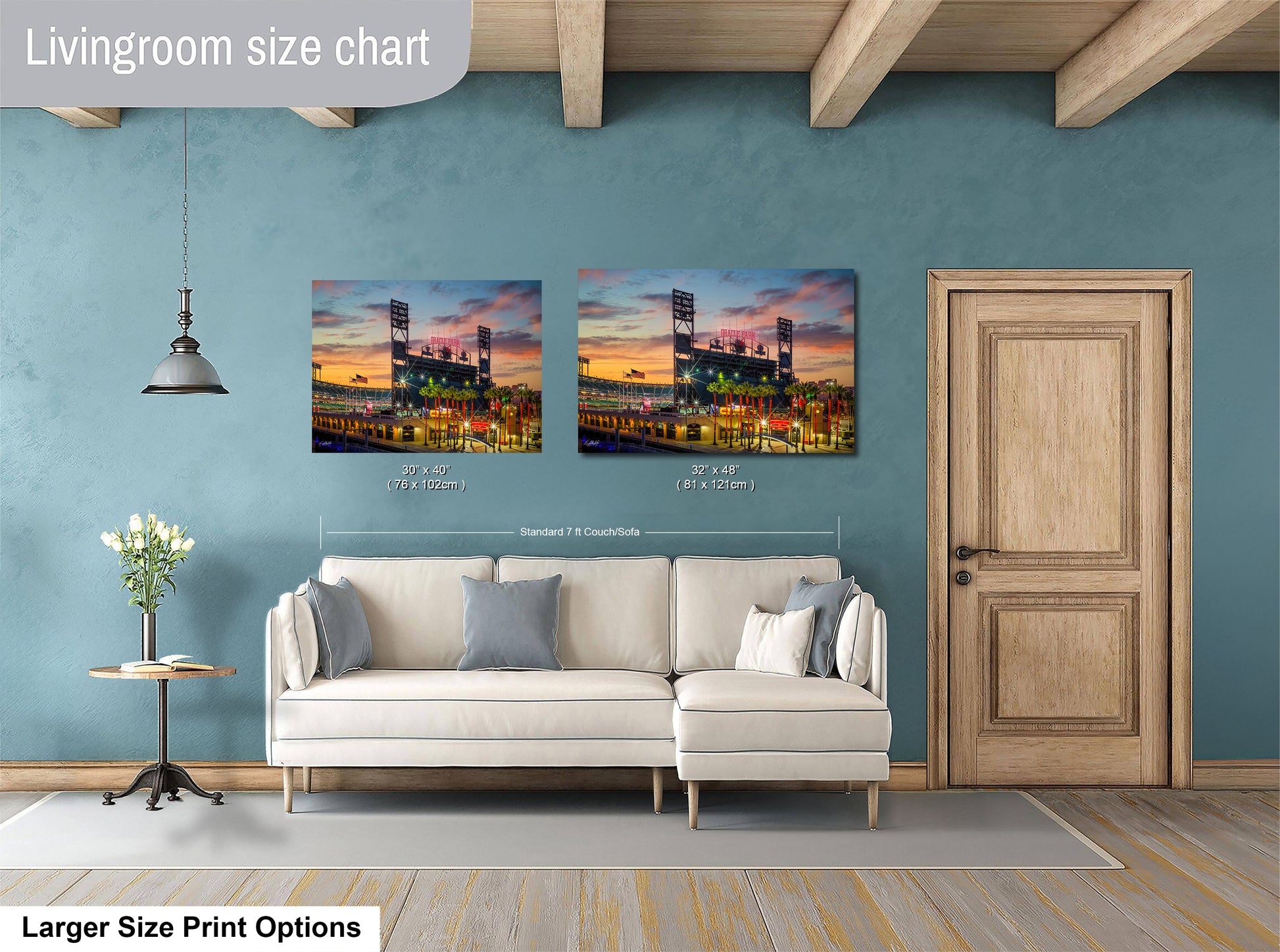 a living room with a white sofa and a wooden door. Above the sofa, there are two framed pictures of a baseball stadium at sunset, with the left picture being larger than the right one. The living room has a blue wall and a wooden ceiling.