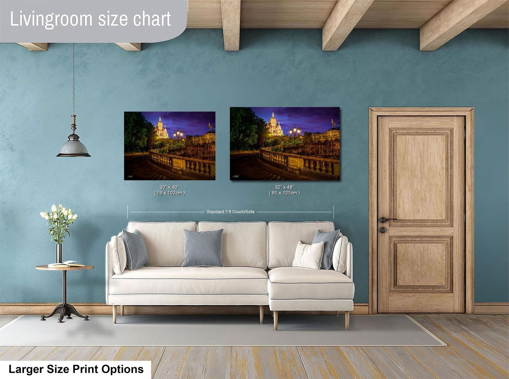 a living room with a white sofa and a wooden door. Above the sofa, there are two framed pictures hanging on the wall, depicting a city street at night with a castle in the background. The living room has a blue wall and a wooden ceiling.