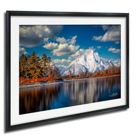 a serene landscape with a mountain range in the background, a calm lake in the foreground, and a forested area with autumn-colored trees.