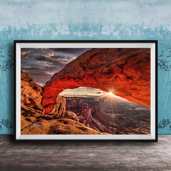 A framed photograph depicting a stunning natural landscape with a large arch formation in the distance, set against a backdrop of a cloudy sky and a sunset.