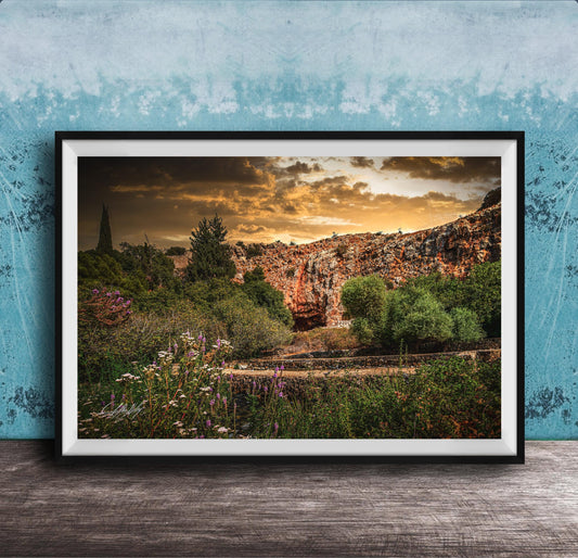 The image is a framed photograph depicting a scenic landscape with a rocky cliff, lush vegetation, and a dramatic sky with clouds.