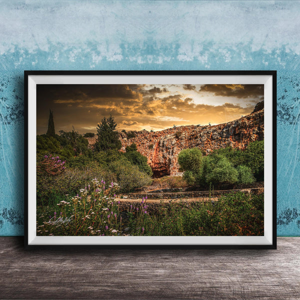 The image is a framed photograph depicting a scenic landscape with a rocky cliff, lush vegetation, and a dramatic sky with clouds.