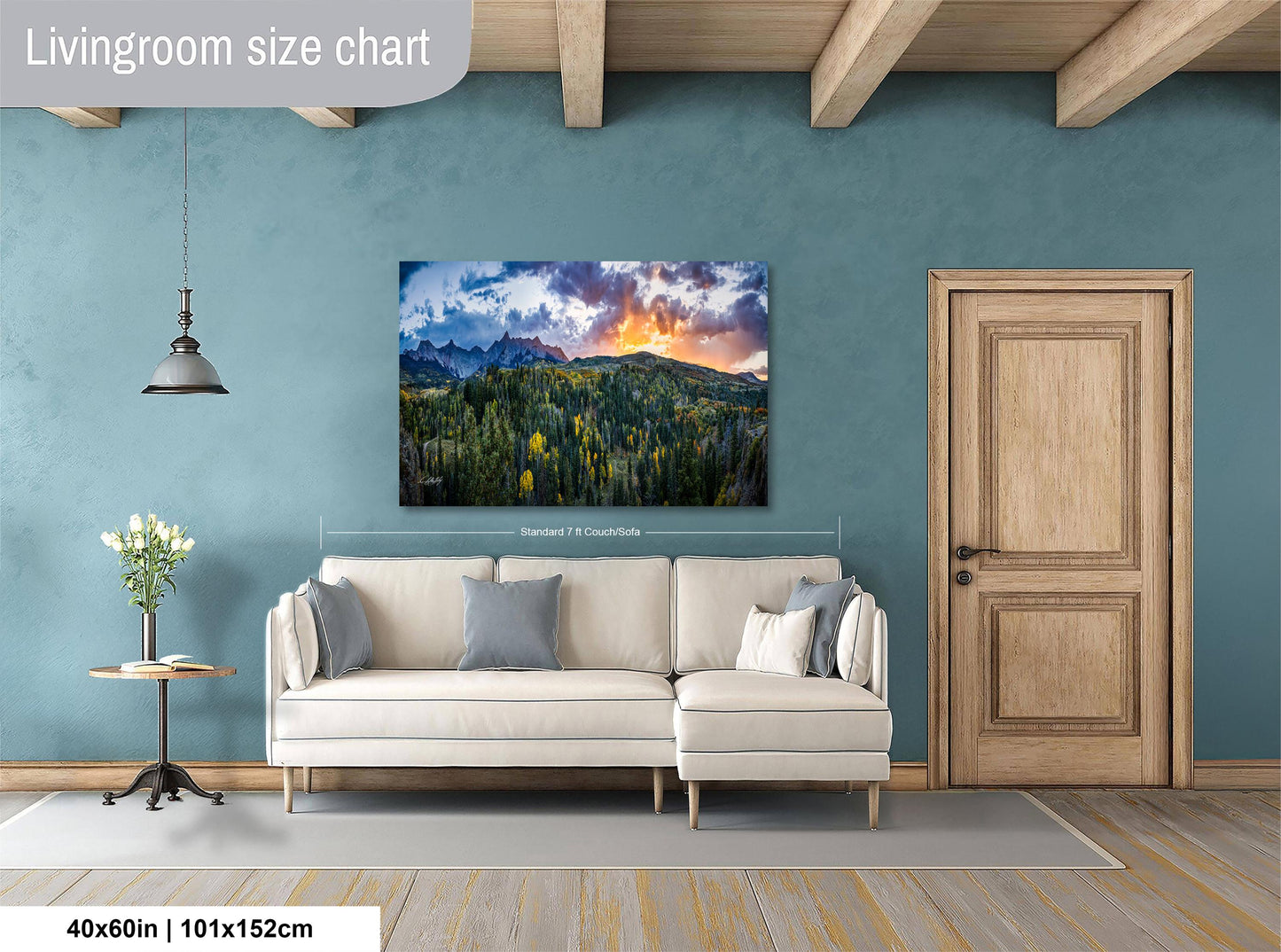 a living room with a large landscape painting hanging on the wall, a white sofa, a wooden door, and a small table with a vase of flowers.