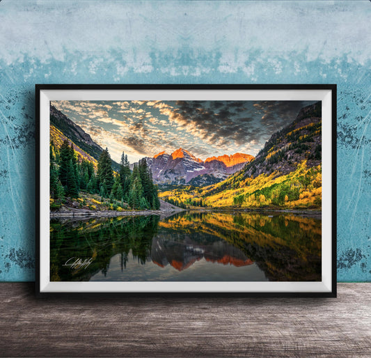 The image is a framed photograph depicting a serene mountain landscape with a lake reflecting the vibrant colors of the sky and surrounding trees.