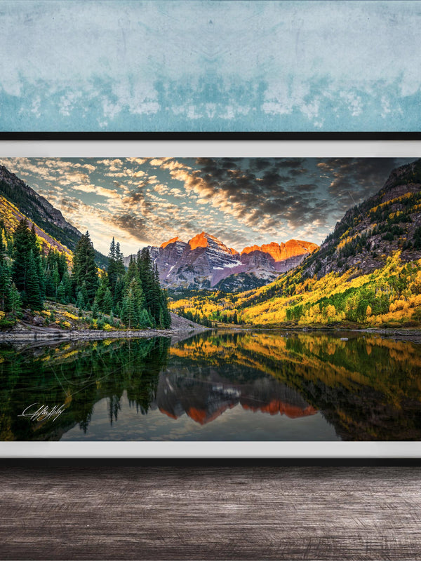 The image is a framed photograph depicting a serene mountain landscape with a lake reflecting the vibrant colors of the sky and surrounding trees.