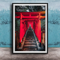 A framed photograph depicting a long, narrow red torii gate leading down a set of stairs, surrounded by lush greenery.