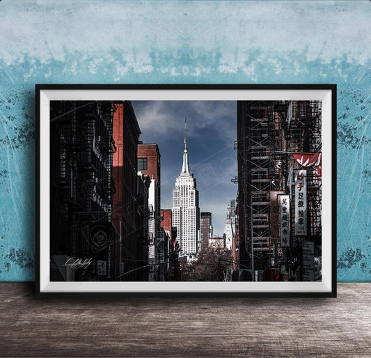 A framed photograph of the iconic Empire State Building in New York City, with the surrounding cityscape visible through the glass facade.