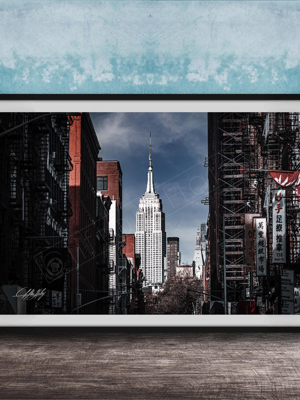 A framed photograph of the iconic Empire State Building in New York City, with the surrounding cityscape visible through the glass facade.