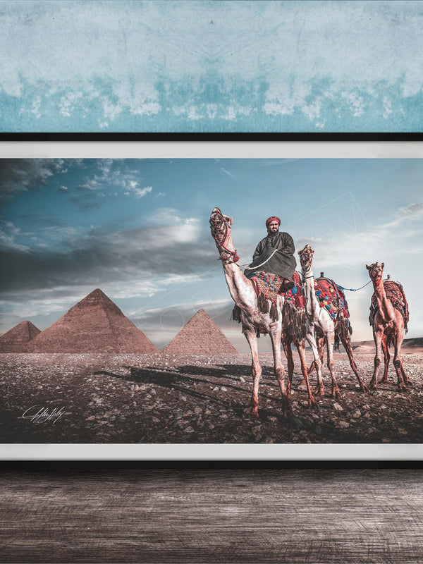 A framed photograph depicting a camel caravan in front of the iconic pyramids of Giza in Egypt.