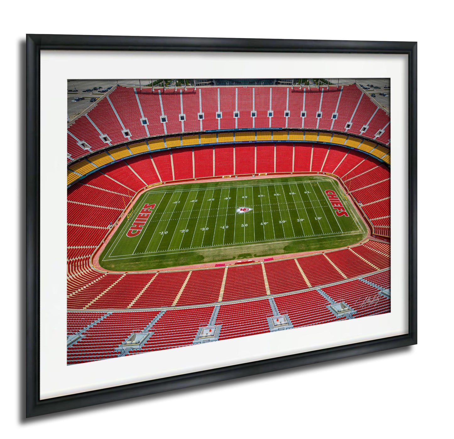 a framed photograph of a football stadium with a large field and rows of red seats.