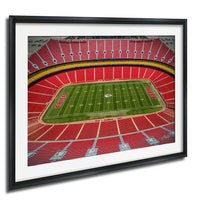 a framed photograph of a football stadium with a large field and rows of red seats.