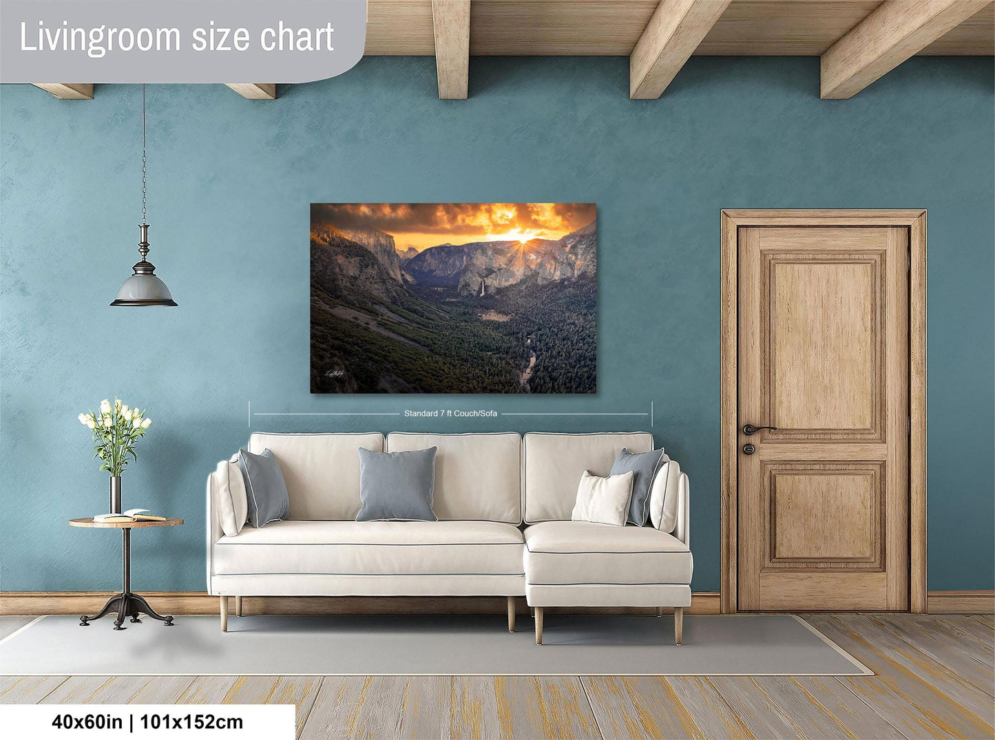 a living room with a large wall painting of a mountainous landscape, a white sofa, a wooden door, and a small table with a vase of flowers.