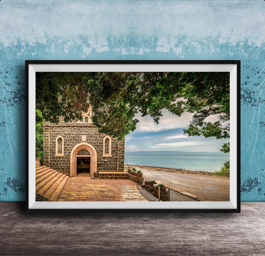 A framed photograph depicting a stone building with arched windows and a stone walkway leading to a beach with a blue sky and trees in the background.