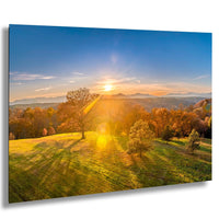a serene landscape with a sunlit field, trees with autumn foliage, and a distant mountain range under a clear blue sky.