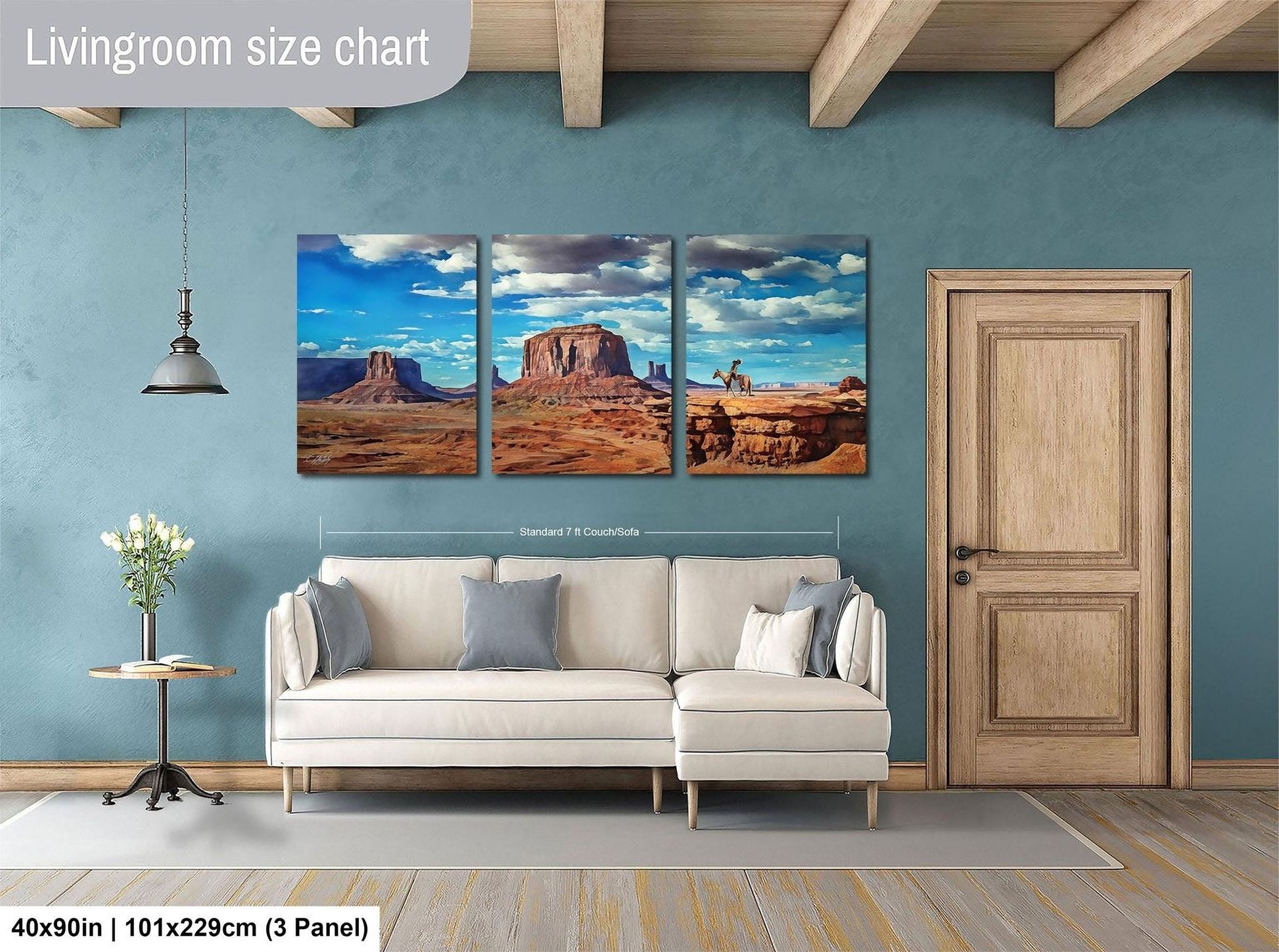 The image is a living room with a large wall art depicting three desert scenes, including a mountain range and a desert landscape. The wall art is mounted above a white sofa, and there is a wooden door and a small table with a vase of flowers in the room.