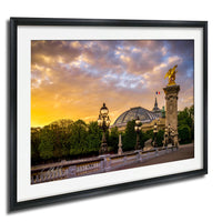 a picturesque scene of a cityscape with a large domed building, ornate street lamps, and a golden statue of a winged figure, all set against a vibrant sunset sky.
