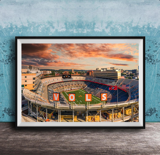 A framed photograph of a sports stadium with the word "VOLS" prominently displayed, set against a backdrop of a colorful sunset sky.