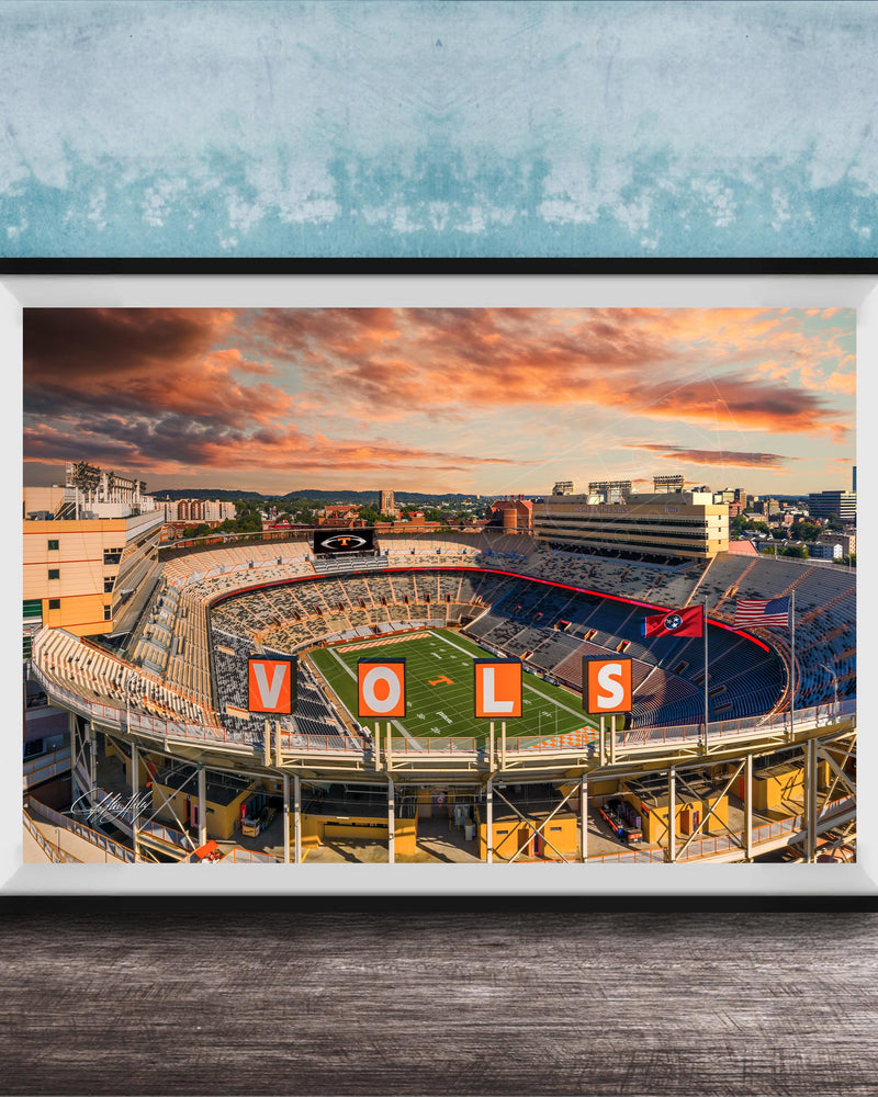 A framed photograph of a sports stadium with the word "VOLS" prominently displayed, set against a backdrop of a colorful sunset sky.