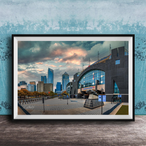 A framed photograph of a cityscape with tall buildings, a large arch structure, and a cloudy sky in the background.