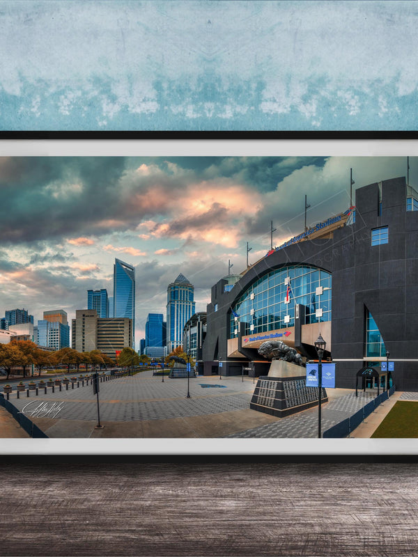 A framed photograph of a cityscape with tall buildings, a large arch structure, and a cloudy sky in the background.