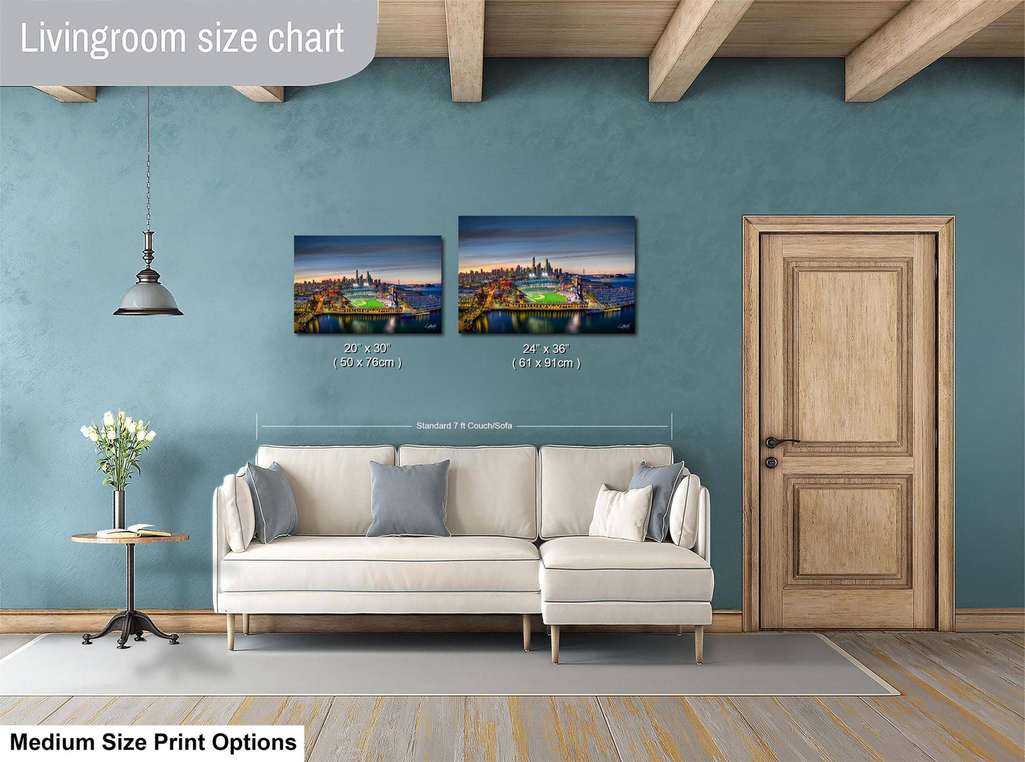 a living room with a white sofa and a wooden door. Above the sofa, there are two framed pictures hanging on the wall, depicting a cityscape. The living room appears to be well-lit and decorated, with a potted plant and a vase on a side table.