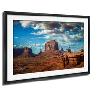 a picturesque desert landscape with towering red rock formations, a lone cowboy on horseback, and a dramatic cloudy sky.
