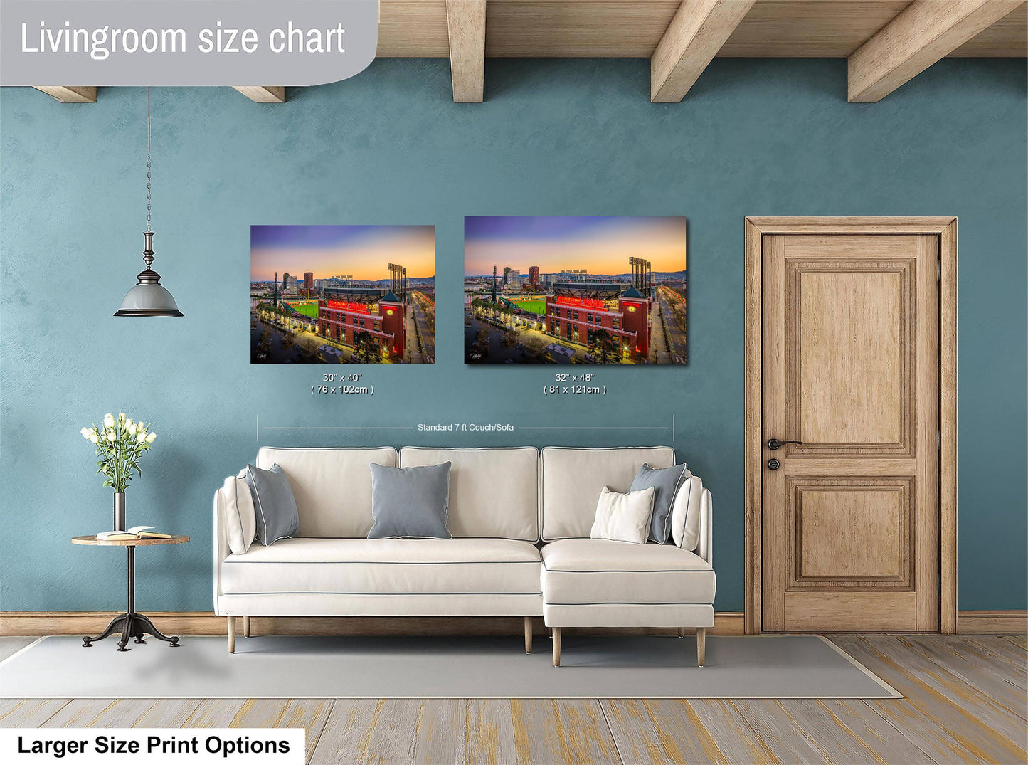 a living room with a white sofa and a wooden door. There are two framed pictures hanging on the wall, depicting a cityscape at sunset. The living room appears to be well-lit and decorated, with a potted plant and a vase adding to the ambiance.