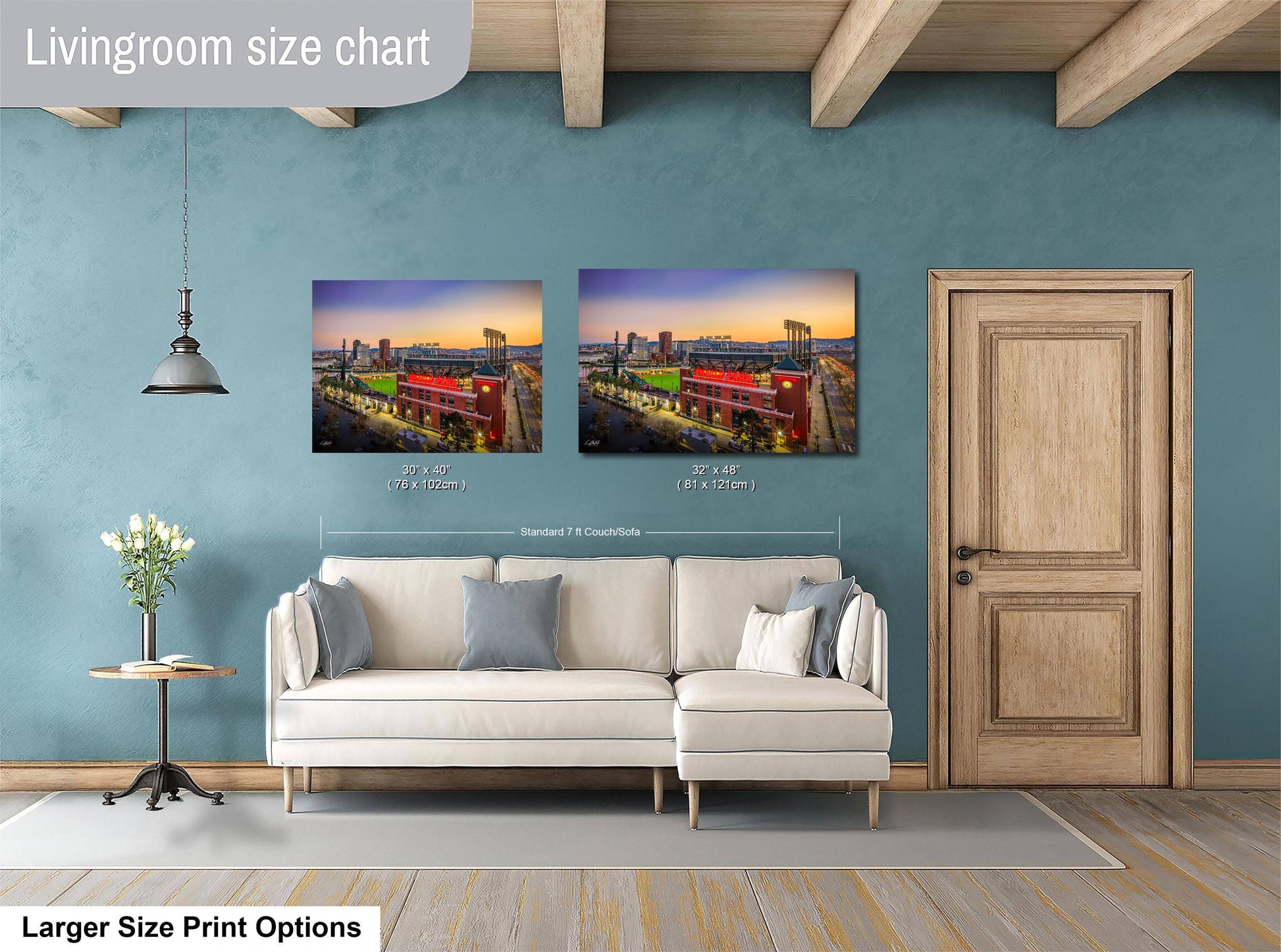 a living room with a white sofa and a wooden door. There are two framed pictures hanging on the wall, depicting a cityscape at sunset. The living room appears to be well-lit and decorated, with a potted plant and a vase adding to the ambiance.