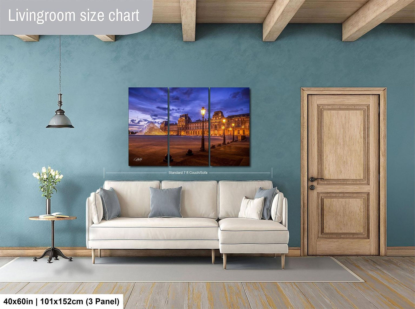The image is a living room with a large, high-quality, three-panel print of a cityscape at night. The print is mounted on the wall above a white sofa, and there is a wooden door and a small table with a vase of flowers nearby. The print is approximately 40 inches wide and 101.5 inches tall, with a 3-panel layout.