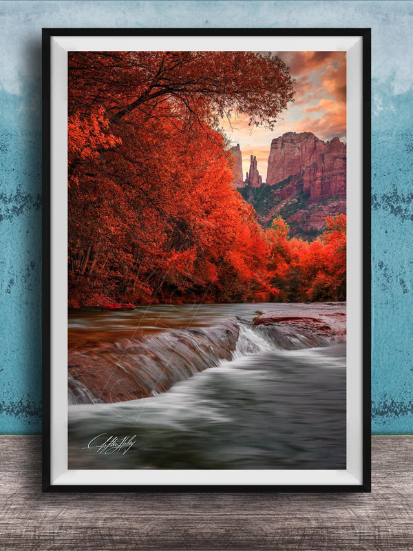 A framed photograph depicting a serene landscape with a waterfall cascading over rocks, surrounded by vibrant red foliage and set against a backdrop of towering red rock formations.