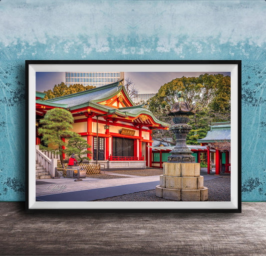 A framed photograph of a traditional Japanese temple with a red roof and white walls, surrounded by trees and a stone fountain.