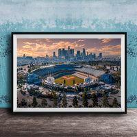 An aerial view of a baseball stadium with the city skyline in the background, framed in a black frame and displayed on a wooden surface.