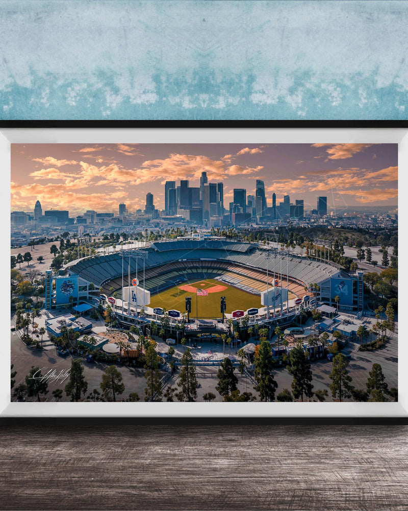 An aerial view of a baseball stadium with the city skyline in the background, framed in a black frame and displayed on a wooden surface.