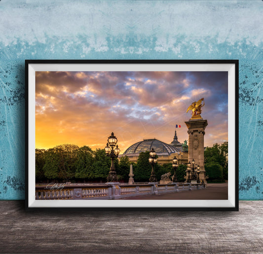 a picturesque scene of a cityscape with a large domed building, ornate lampposts, and a statue of a winged figure, all set against a vibrant sunset sky.