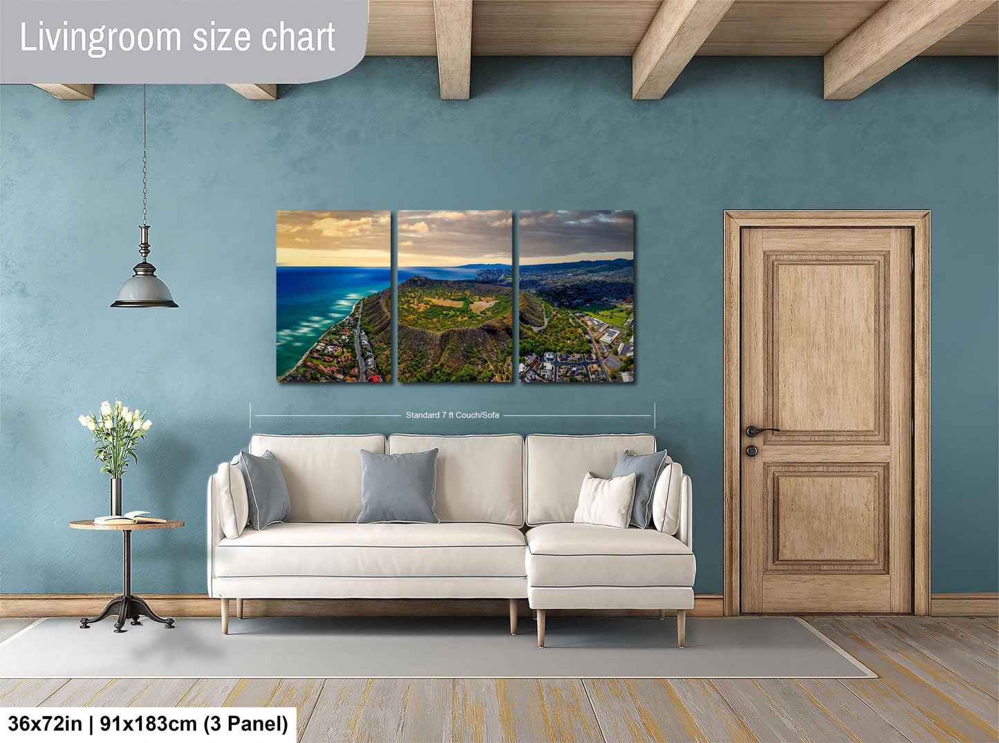 The image is a living room with a large wall art depicting a scenic coastal landscape. The living room has a white sofa and a wooden door, and the wall art is approximately 36 inches wide and 15 inches tall.
