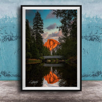 A framed photograph depicting a scenic landscape with a bridge, trees, and a mountain in the background, reflecting in a body of water.
